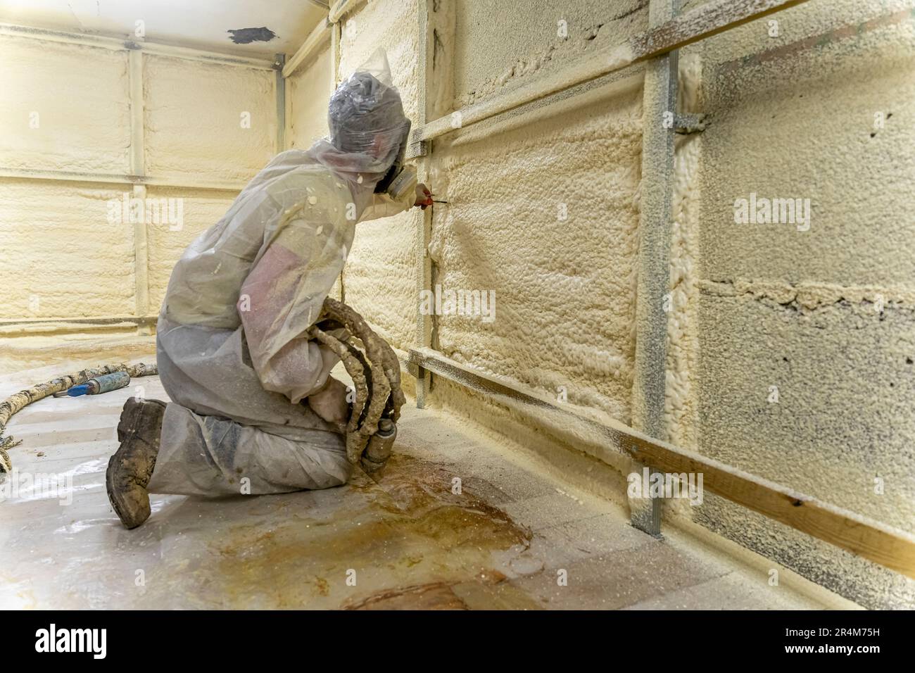 worker in a protective suit insulates the walls with polyurethane foam ...