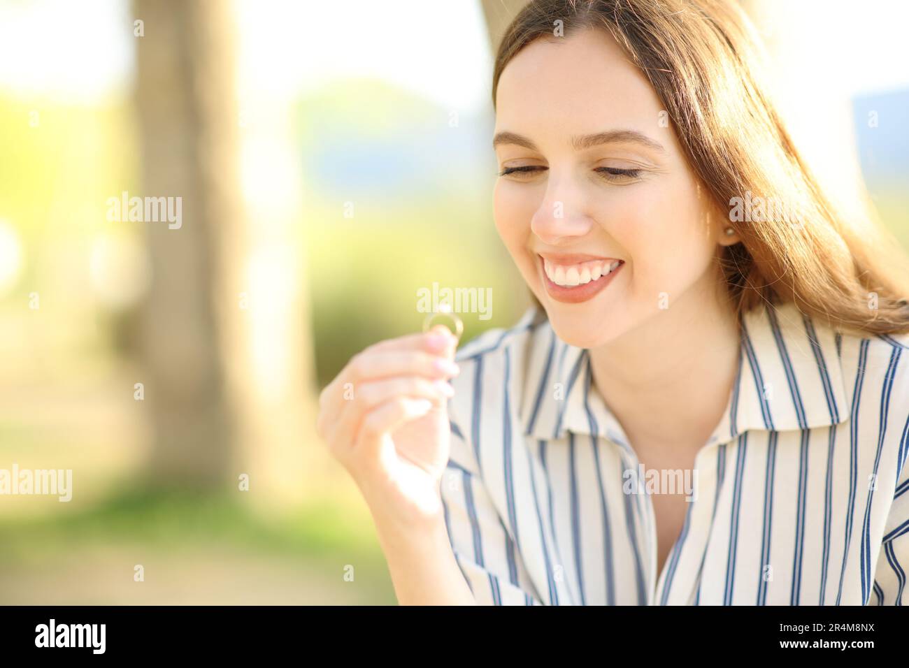 Happy fiancee looking at engagement ring in nature Stock Photo