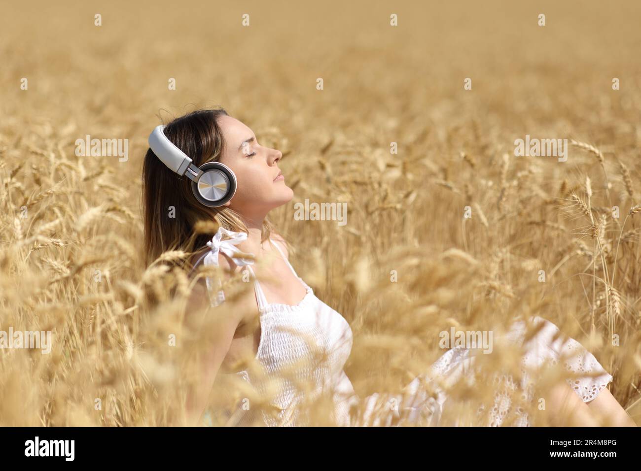 Profile of a relaxed woman with headphone listening audio sitting in a field Stock Photo