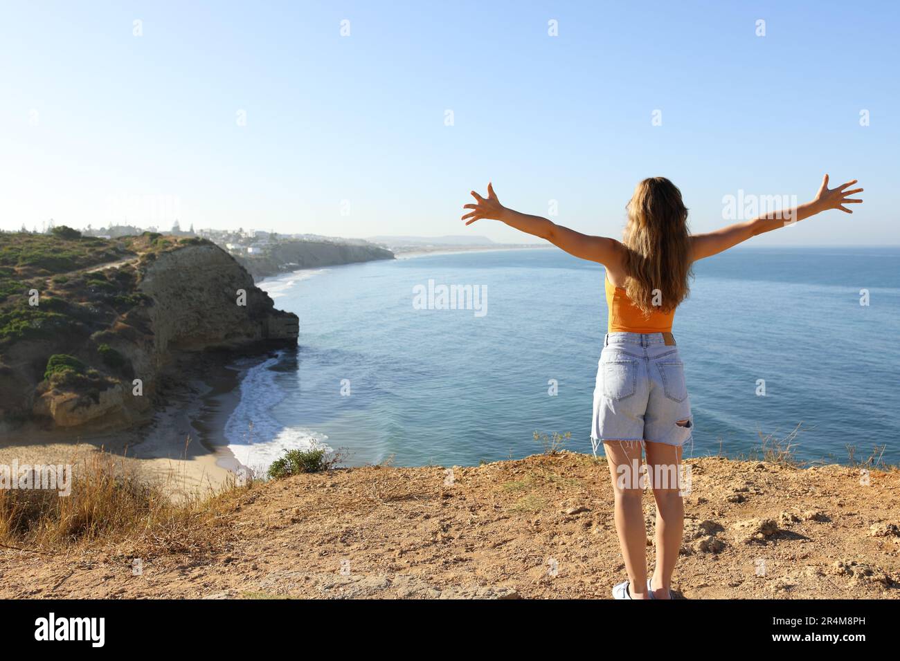 Back view portrait of an excited woman celebrating vacation in a coast outstretching arms Stock Photo