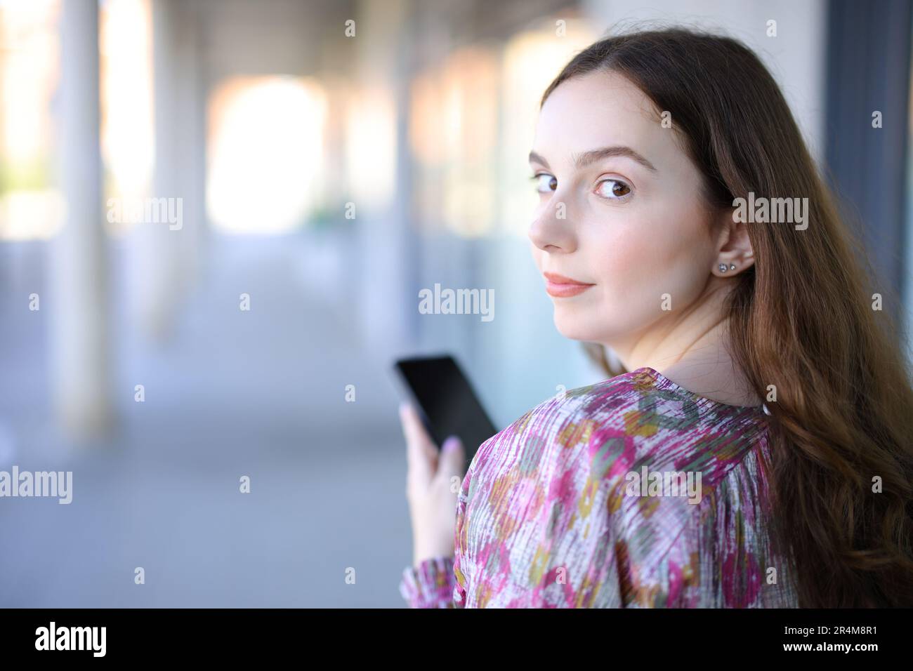 Serious woman using smart phone twirling looking at you in the street Stock Photo