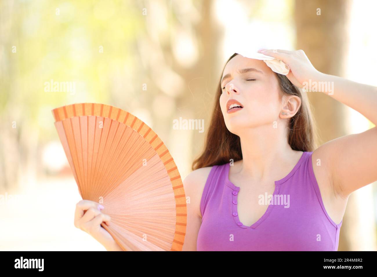 Stressed woman drying sweat with a tissue and fanning a hot summer day Stock Photo