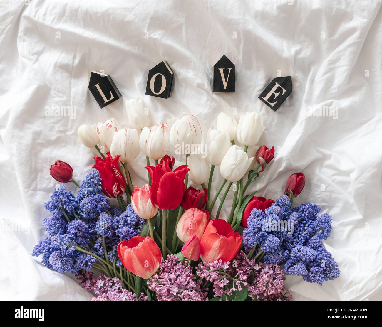A bouquet of fresh flowers and a decorative word Love in a white bed — free download