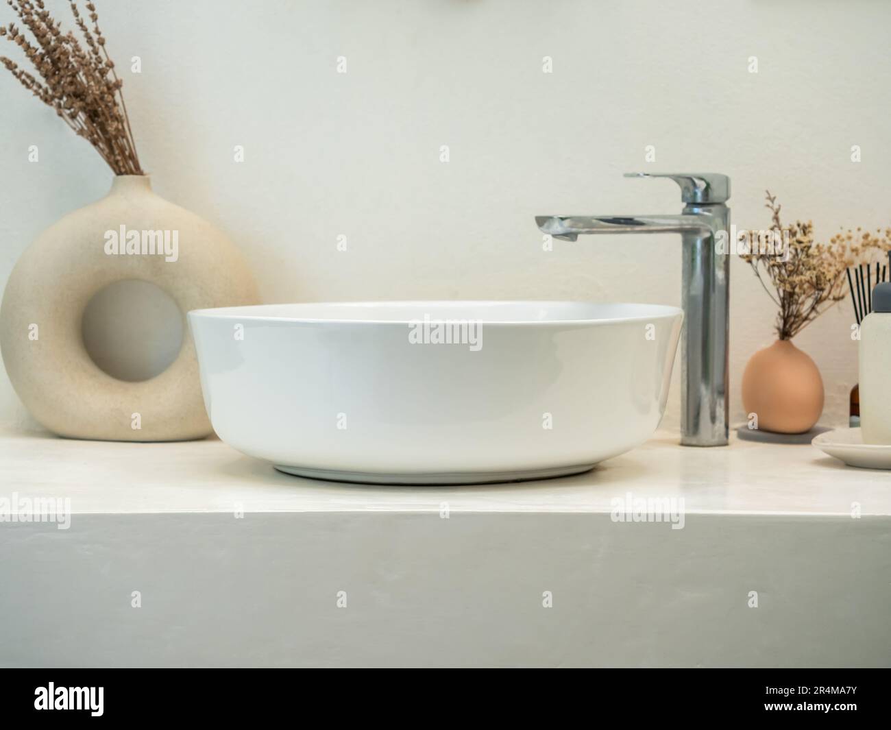 Clean minimal style powder room or bathroom interior with modern round sink basin, faucet, green leaves in modern design pots on marble shelf and whit Stock Photo
