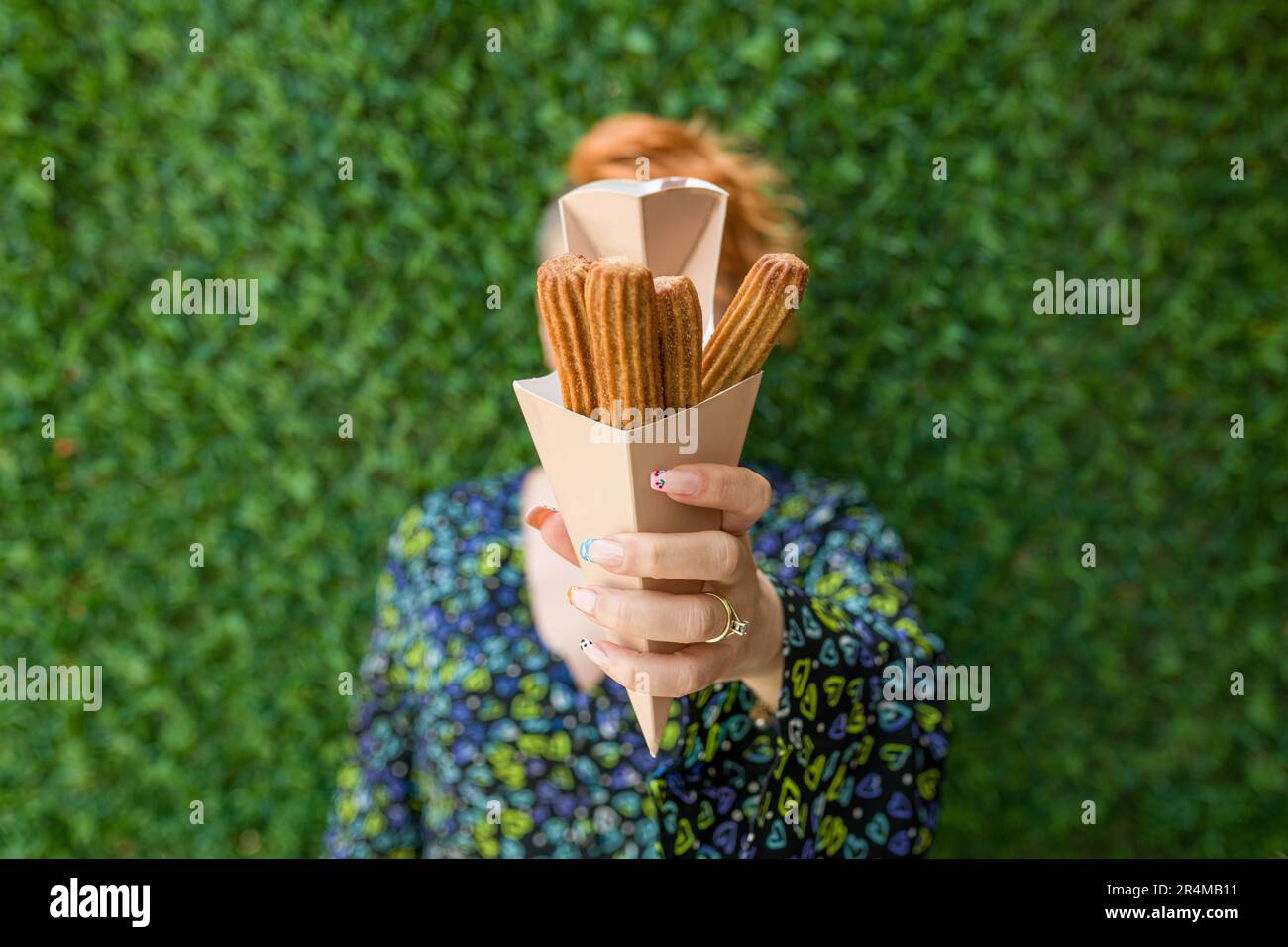 woman holding churros in cardboard box in front of green grass wall Stock Photo