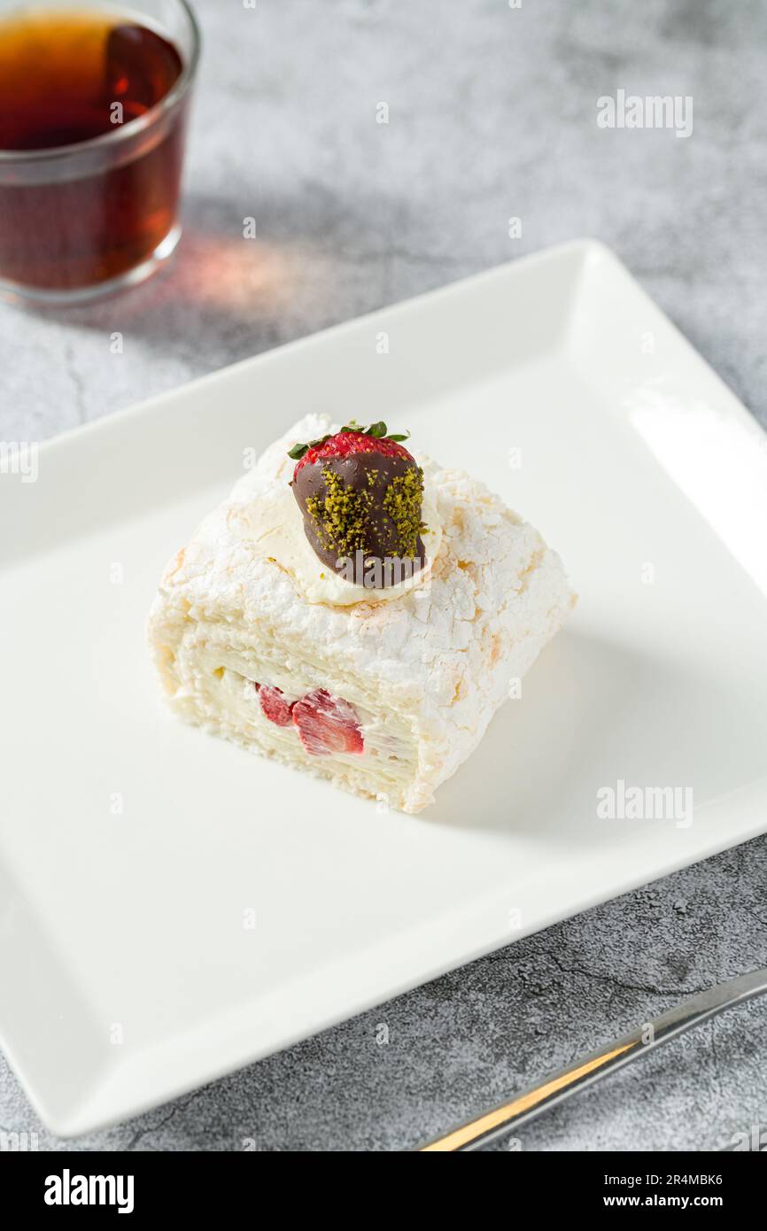 Strawberry roll cake with tea next to it on stone table Stock Photo