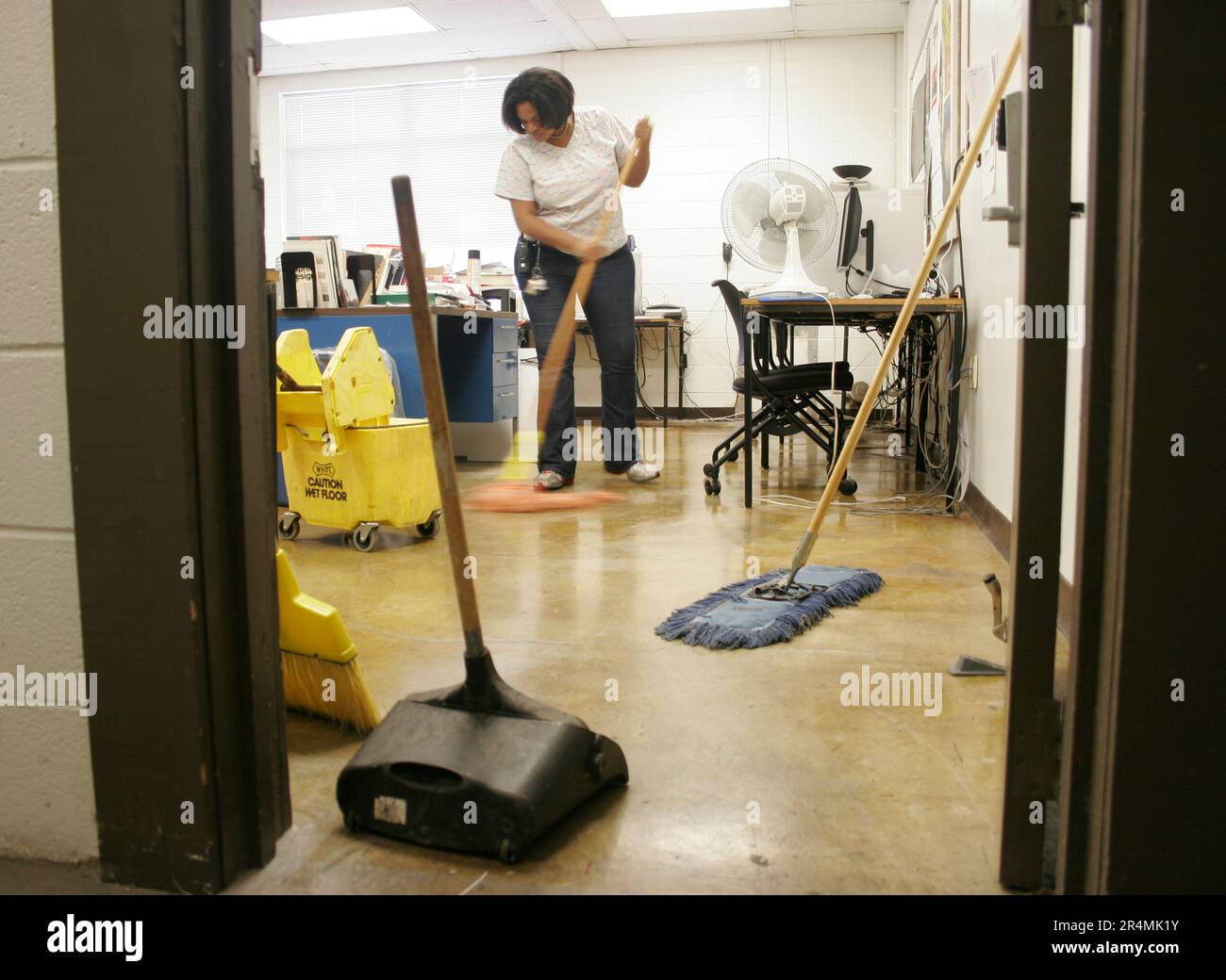 A female janitor sweeps the floor with a broom and dustpan in a