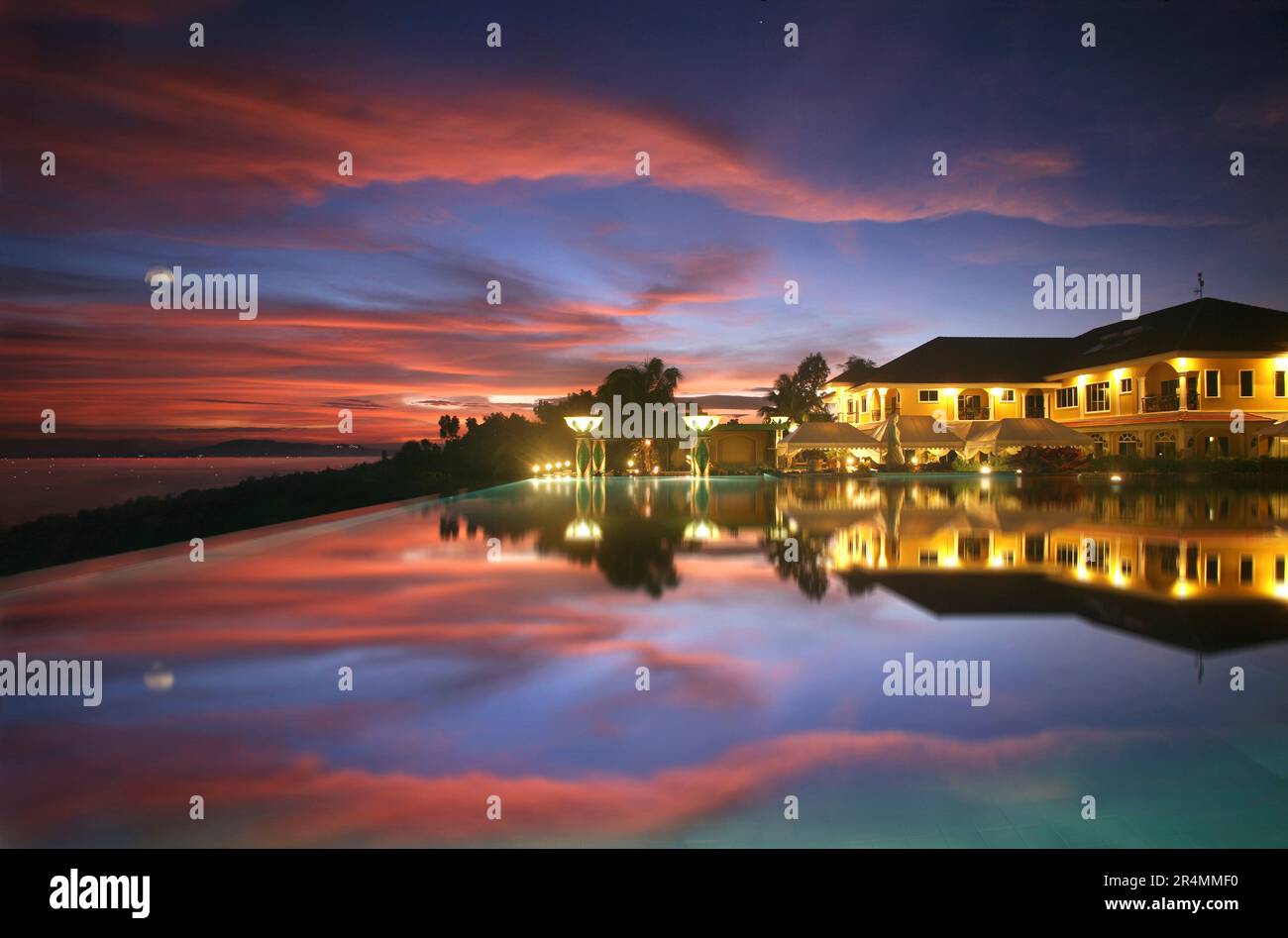 Infinity pool beneath a blue and orange sky beside a hotel resort, lit up in the evening in the Philippines. Stock Photo