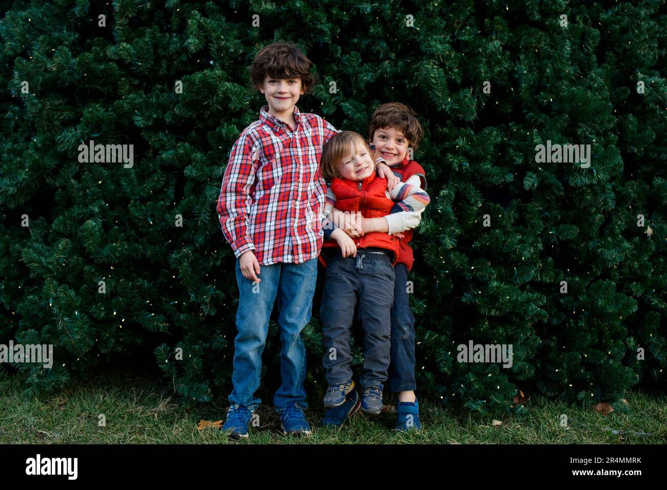 Three playful brothers stand happily together in front of tree Stock Photo