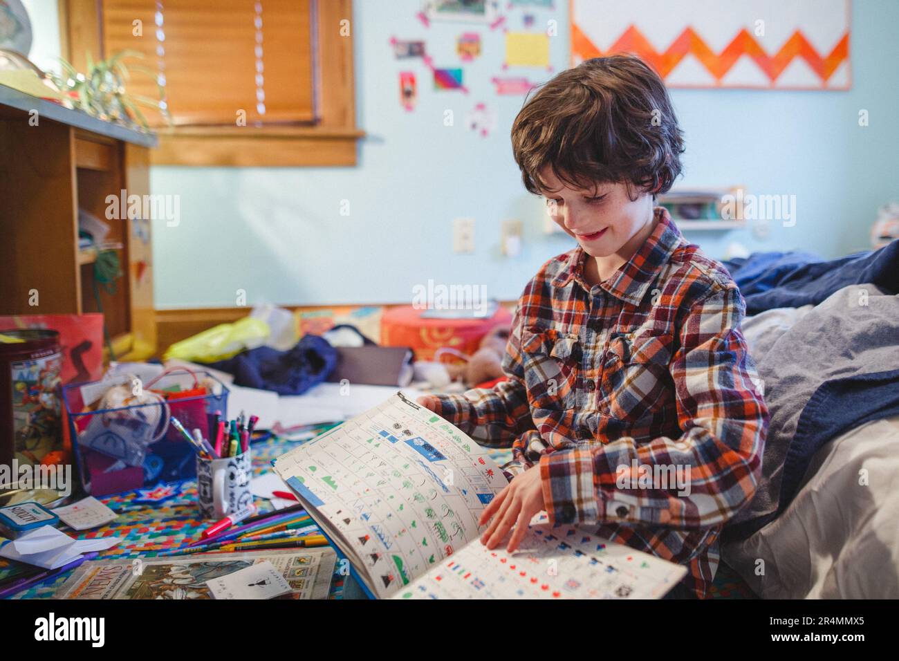 A happy child sits on cluttered floor of his bedroom reading a book Stock Photo
