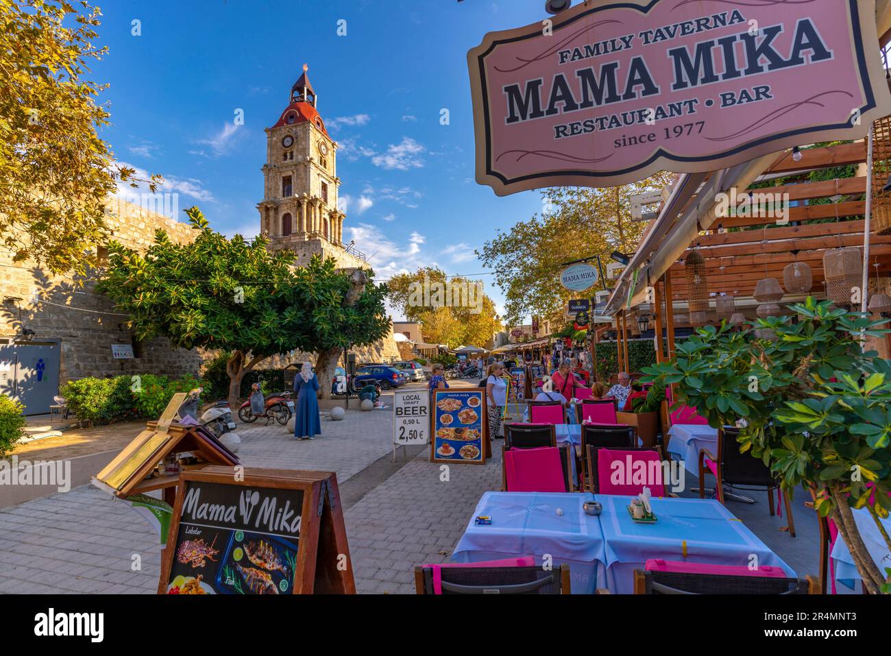 View of Medieval Clock Tower and restaurant tables, Old Rhodes Town, UNESCO World Heritage Site, Rhodes, Dodecanese, Greek Islands, Greece, Europe Stock Photo