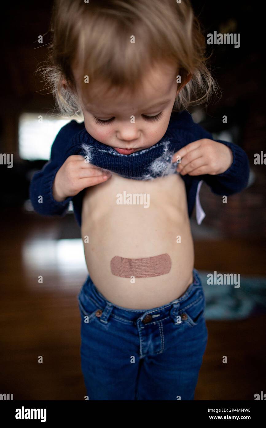 Young toddler girl looking at bandaid on belly Stock Photo