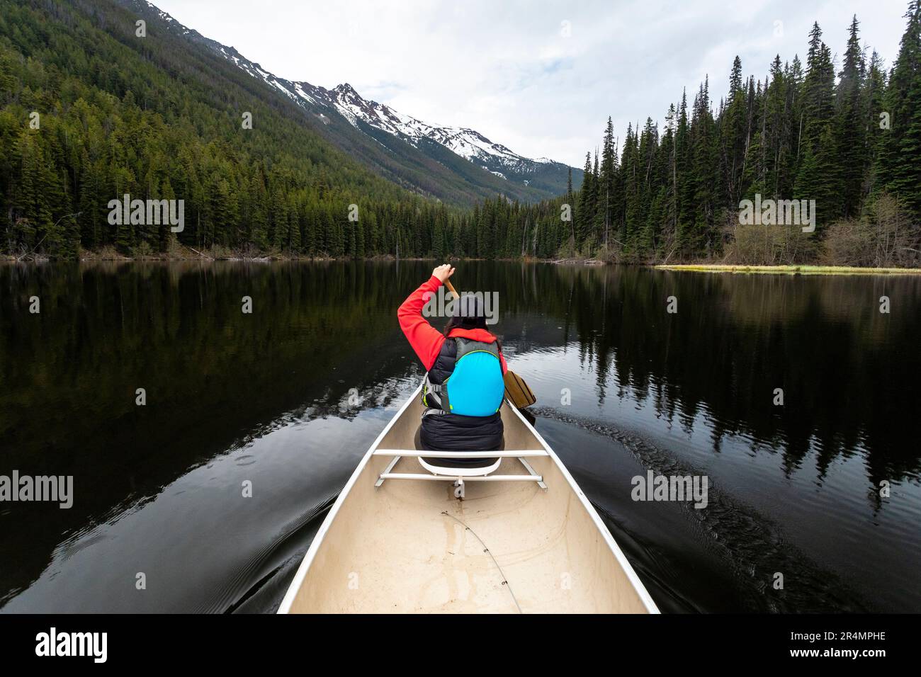 Rear view of woman canoeing on Kingdom Lake with trees and mountains ...