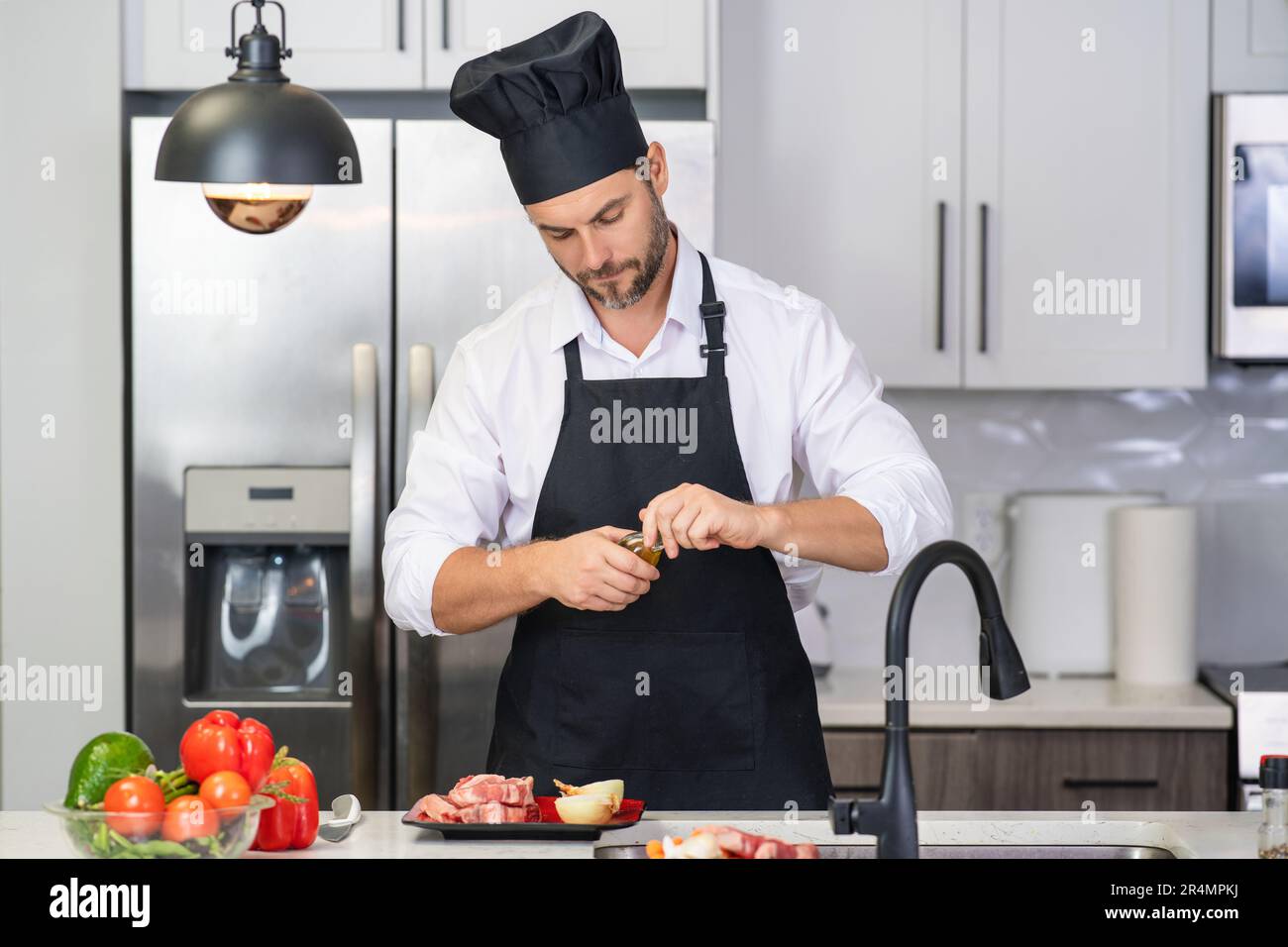 Man in apron and chef hat cooking food in kitchen. Handsome man cooking healthy food in kitchen