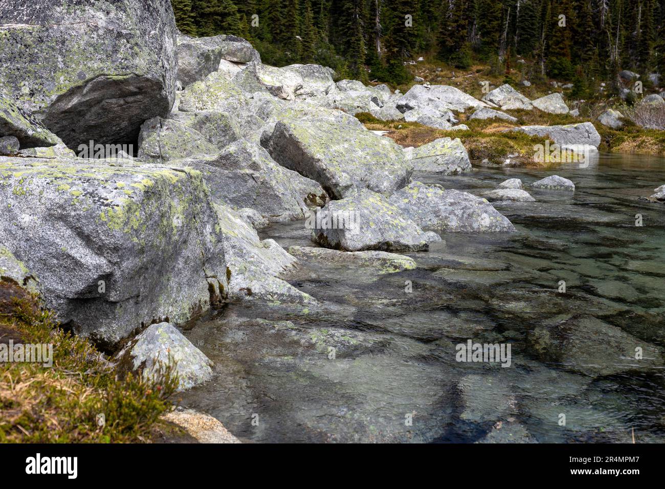 Water flows out from underneath boulders into a lake in the mountains. Stock Photo