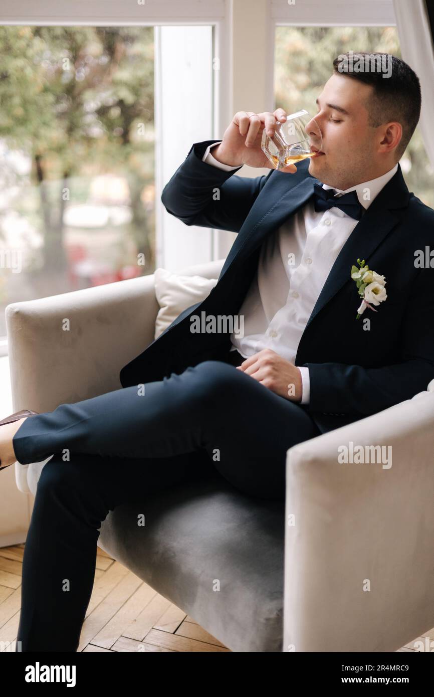 Handsome groom in dark blue suit sitting on chair with glass of whiskey.  Groom's morning. Wedding day Stock Photo - Alamy