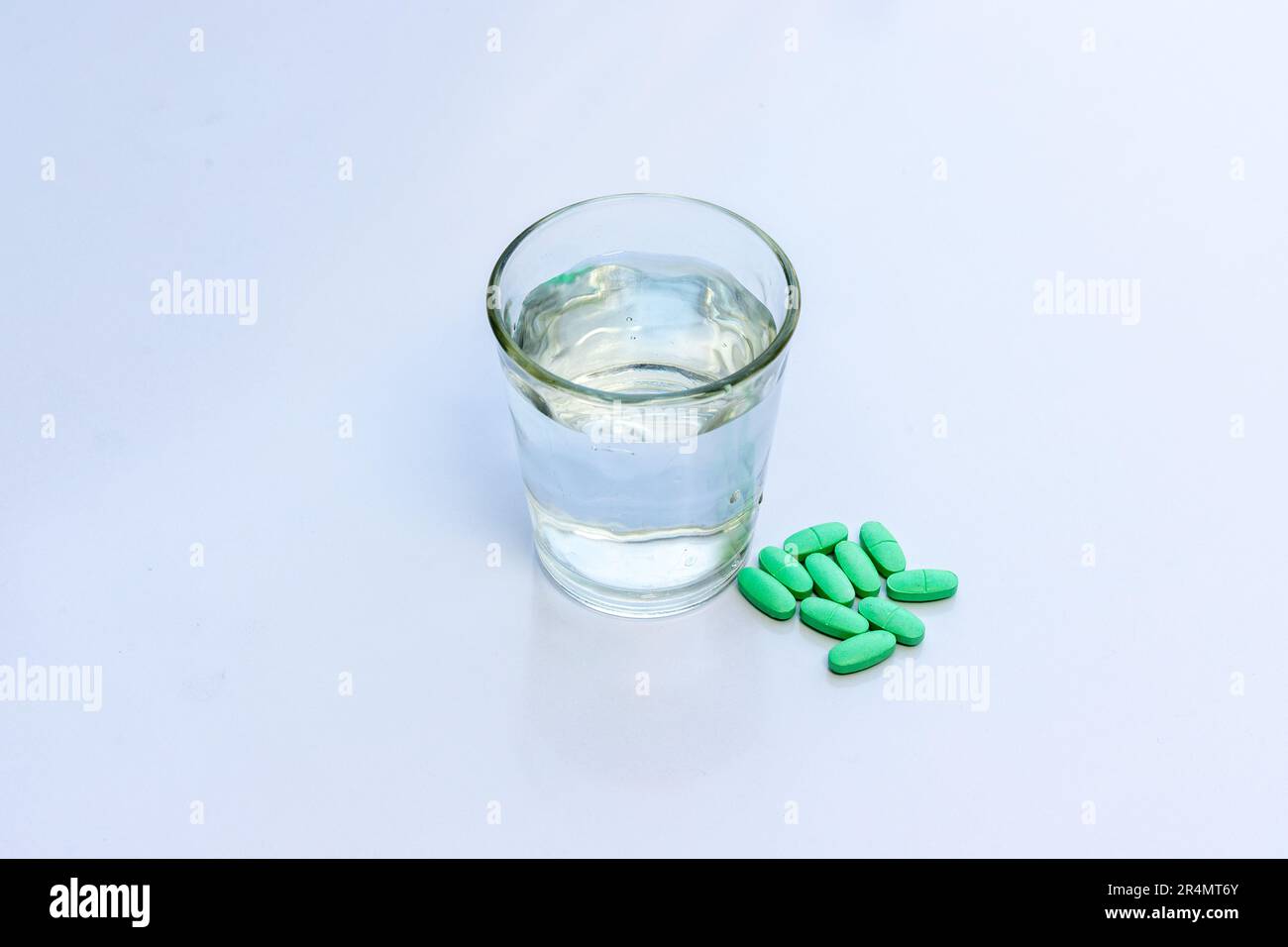 Green pills with a glass of water on white isolated background Stock Photo