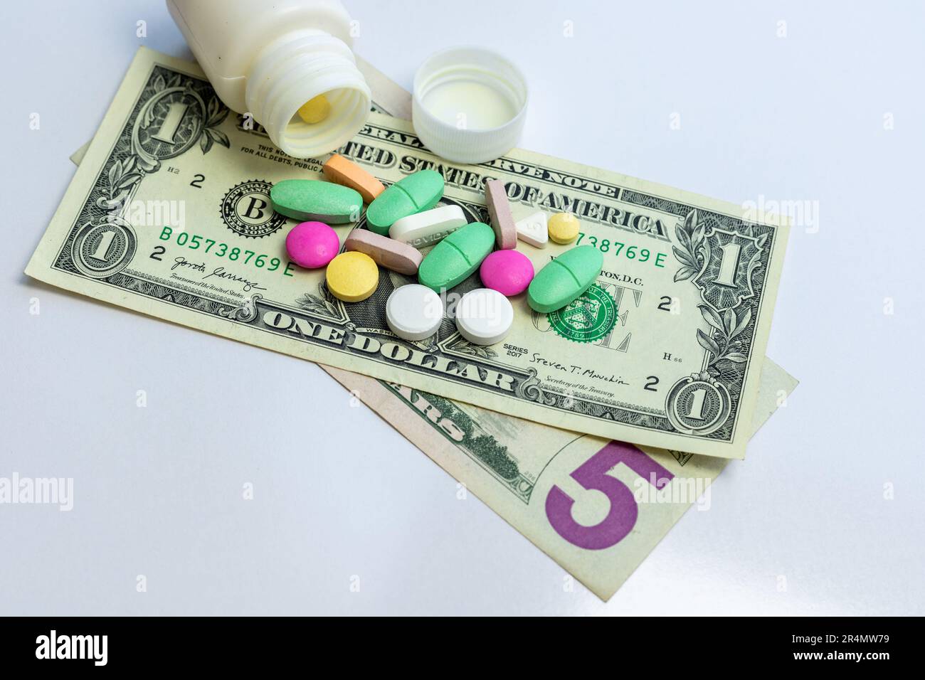 Medicine pills and tablets scattered from a bottle on US dollar bills. Health care expenses concept. Stock Photo