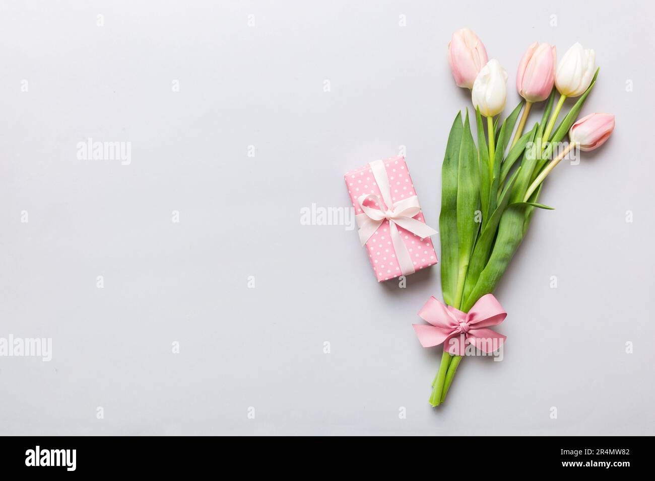 Pink tulips flowers and gift or present box on colored table background. Mothers Day, Birthday, Womens Day, celebration concept. Space for text top vi Stock Photo