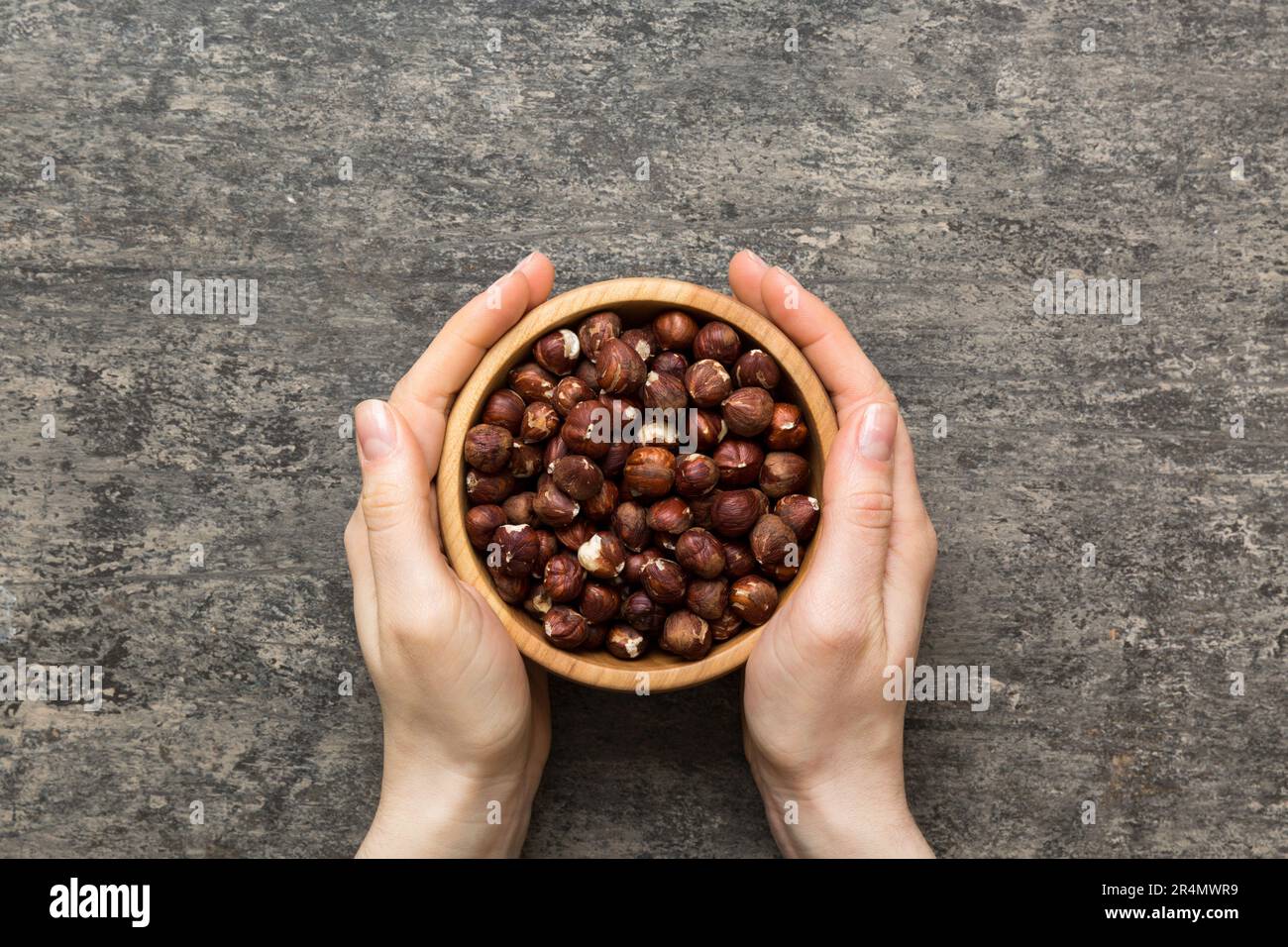 Woman hands holding a wooden bowl with hazelnut nuts. Healthy food and ...