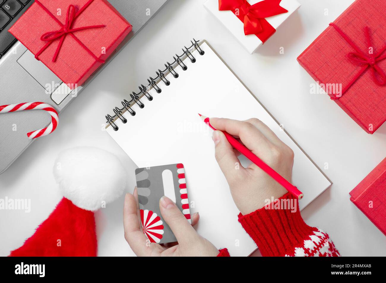 Christmas online shopping flat lay. Girl writing shopping list. Female Hands with Credit card and Pencil. Laptop and christmas presents on white table Stock Photo