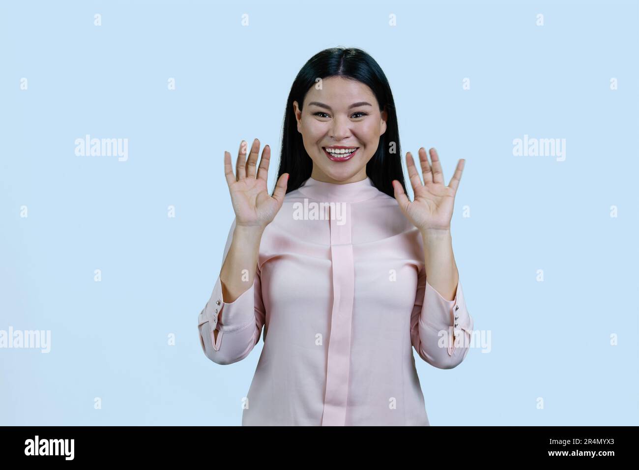 Young asian woman with her hands up shows her palms. Give up gesture. Isolated on pale blue background. Stock Photo