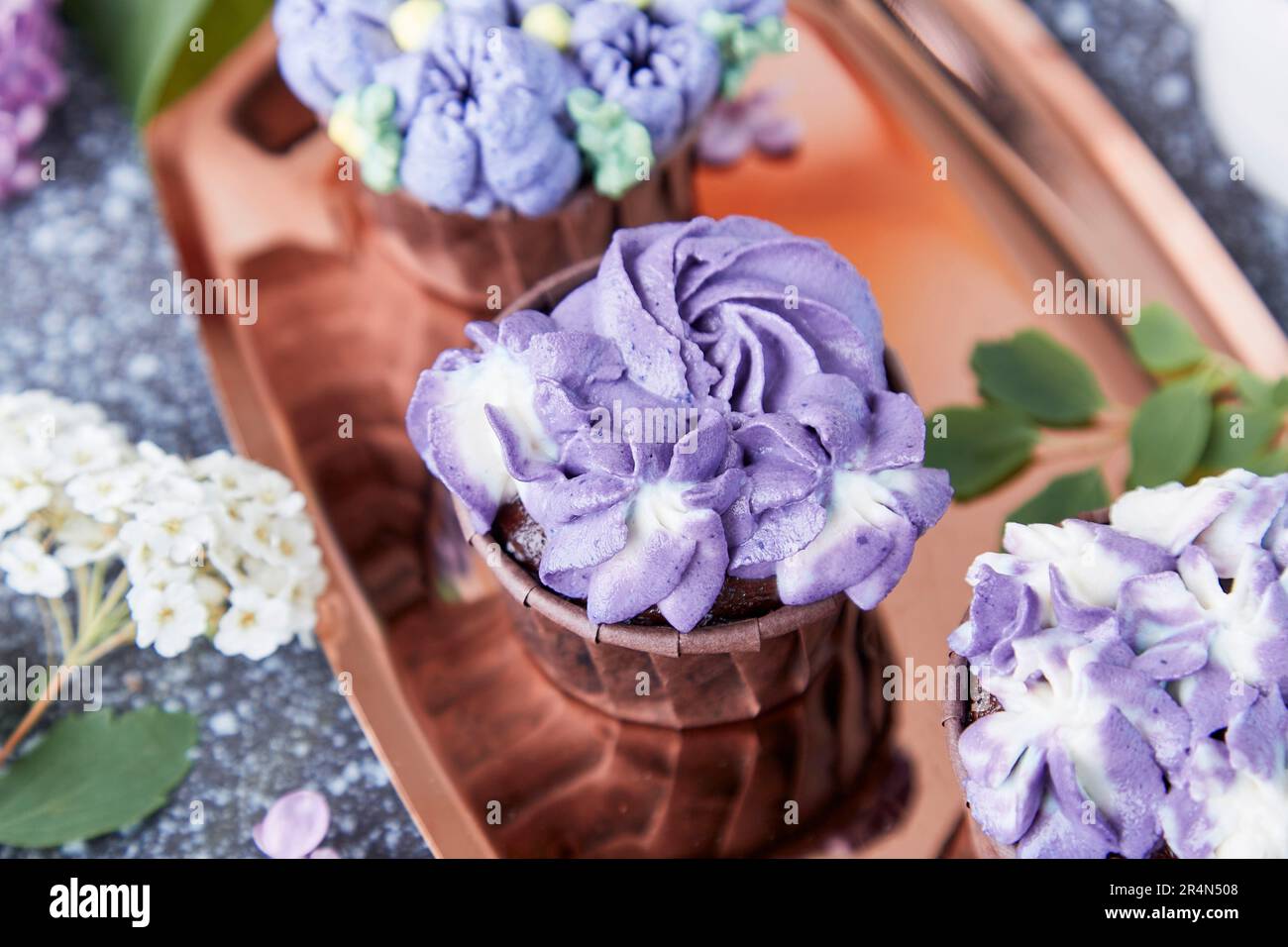 Purple aesthetics trendy floral cupcake on golden tray. Stylish, feminine no sugar dessert close up. Stock Photo