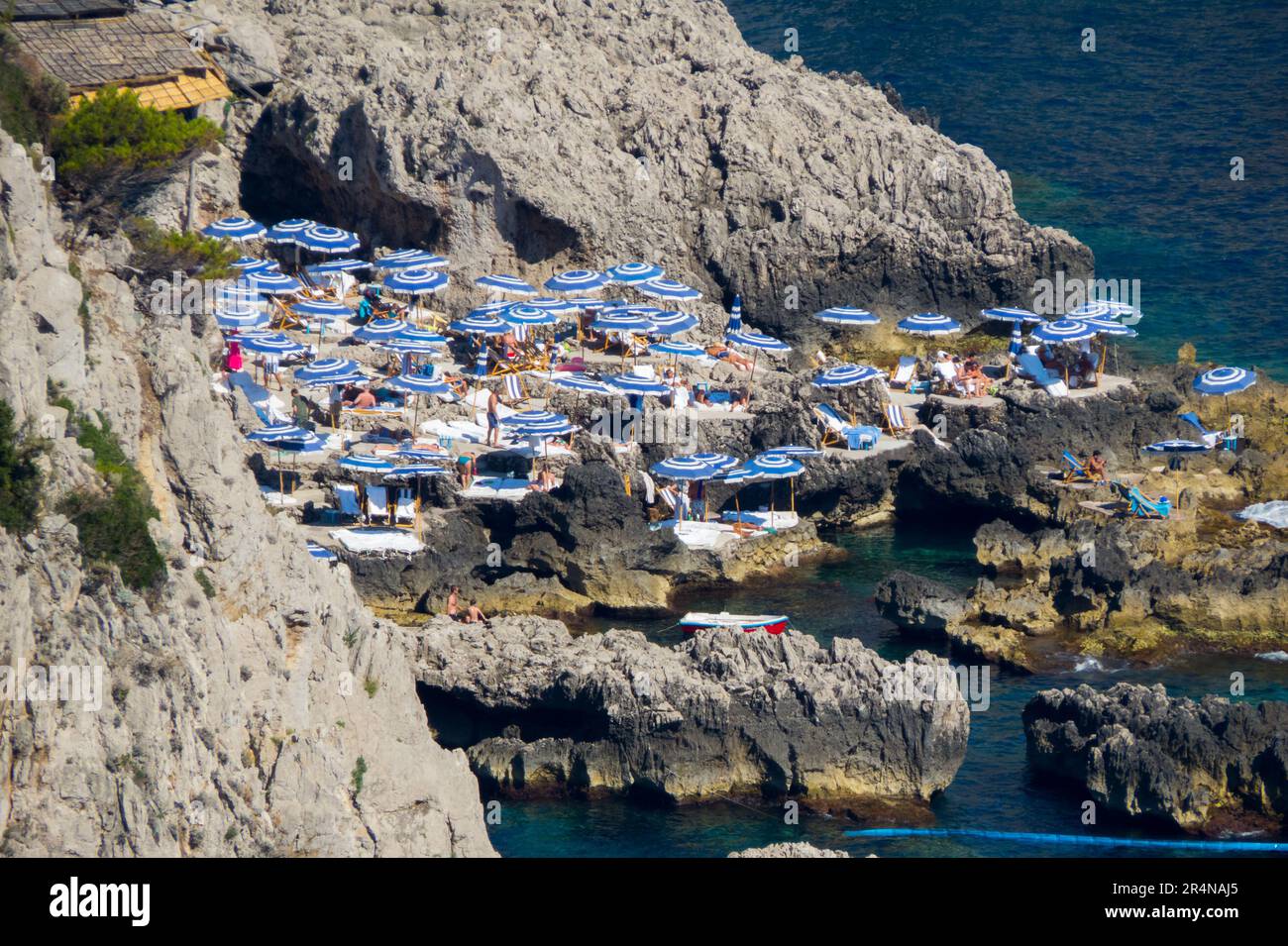 Playa rocosa entre acantilados, desde arriba, llena de sombrillas blancas y azules, en la isla de Capri Stock Photo