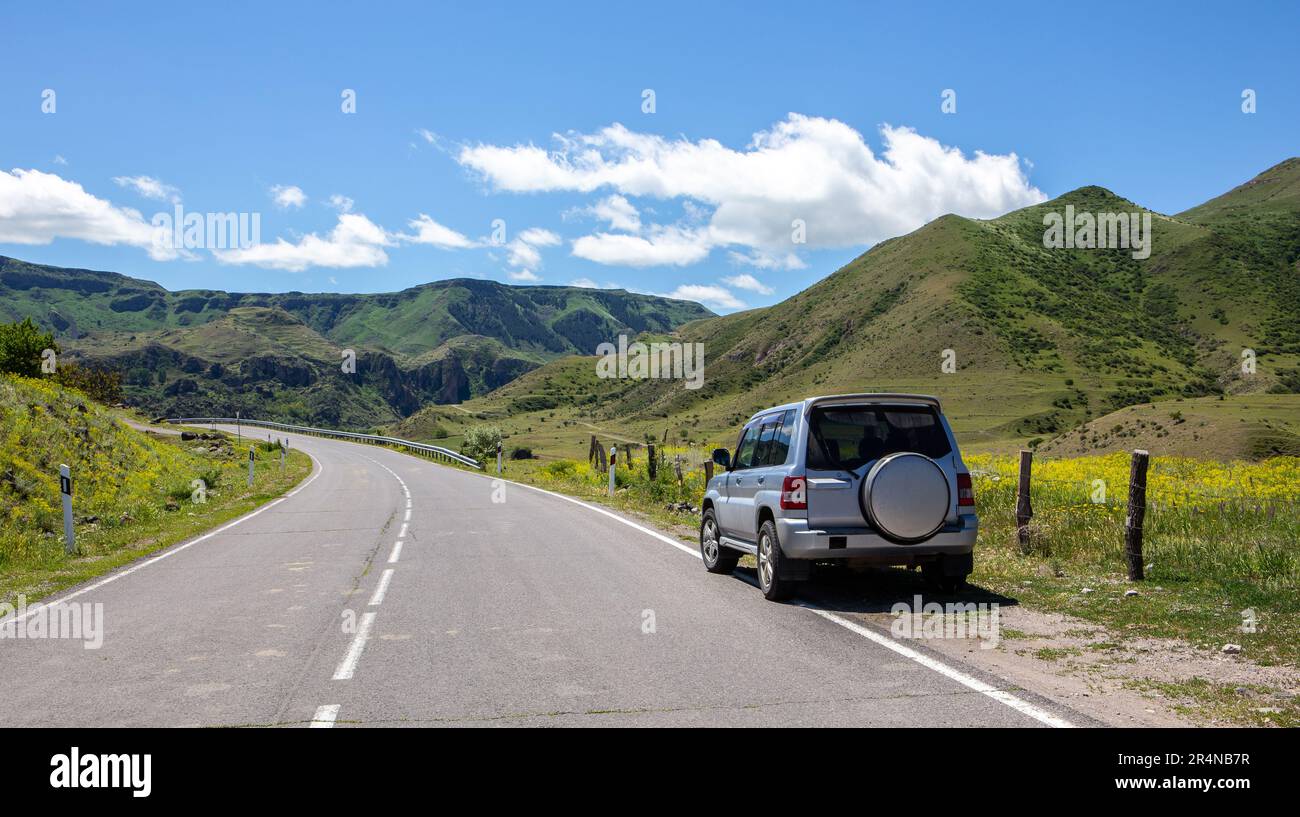 Off-road 4x4 car on a tarmac road in Mtkvari river valley in Samtskhe Javakheti region in Southern Georgia, green grasslands and Caucasus mountains. Stock Photo
