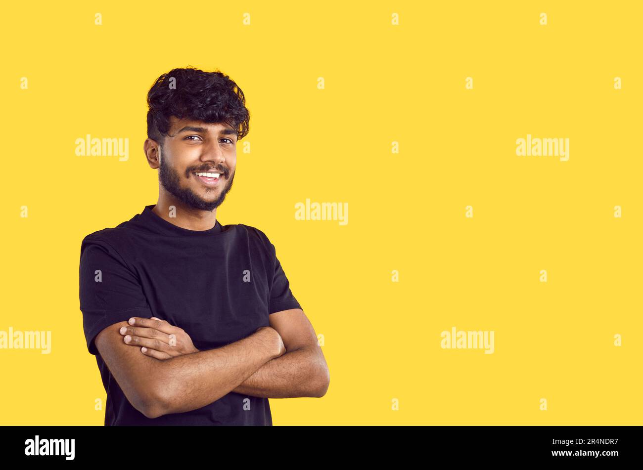 Young Indian man in pose of confident person, smiling crossing arms in front of him stands in studio Stock Photo