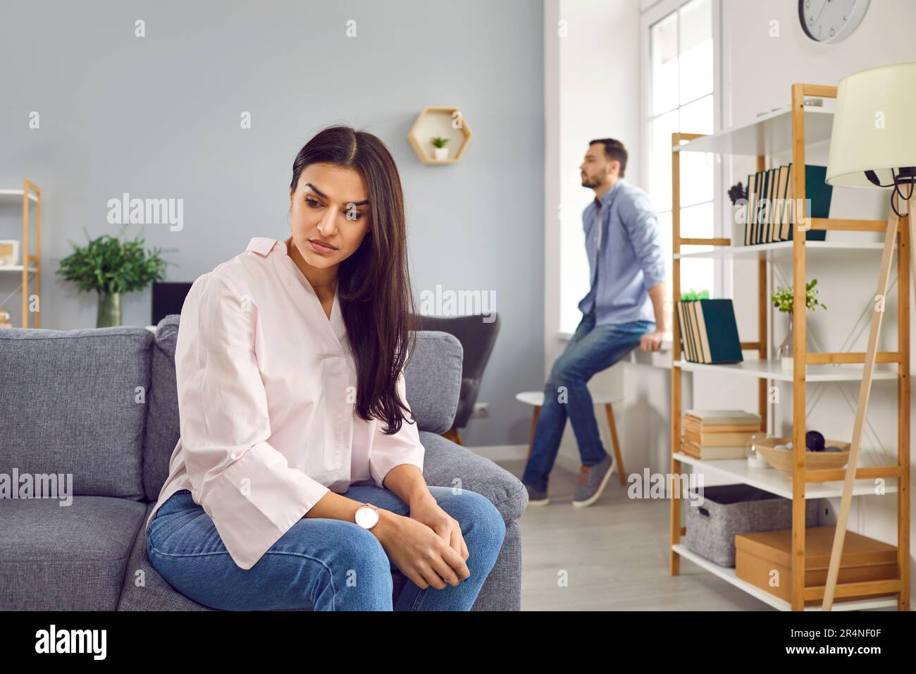 Upset young woman sitting on sofa and a man in background at home. Quarrel and divorce concept. Stock Photo
