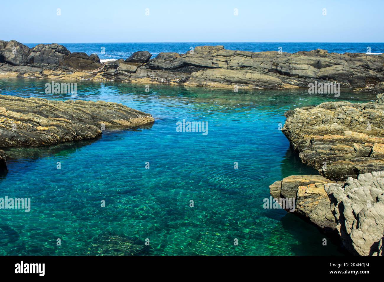 A deep clear rock pool, protected from the ocean by a sharp rocky reef, along the Tsitsikamma Coast of South Africa Stock Photo