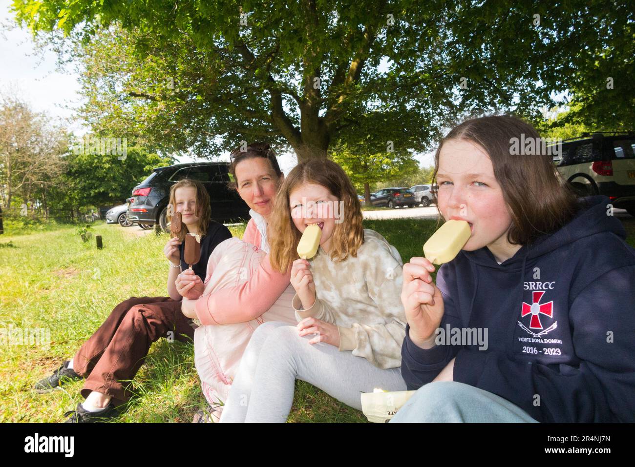 Mum / mother with three daughters in the park, all enjoying an ice cream treat on a hot day. London. UK. Girl / girls ages from 8 year old to 13. (134) Stock Photo