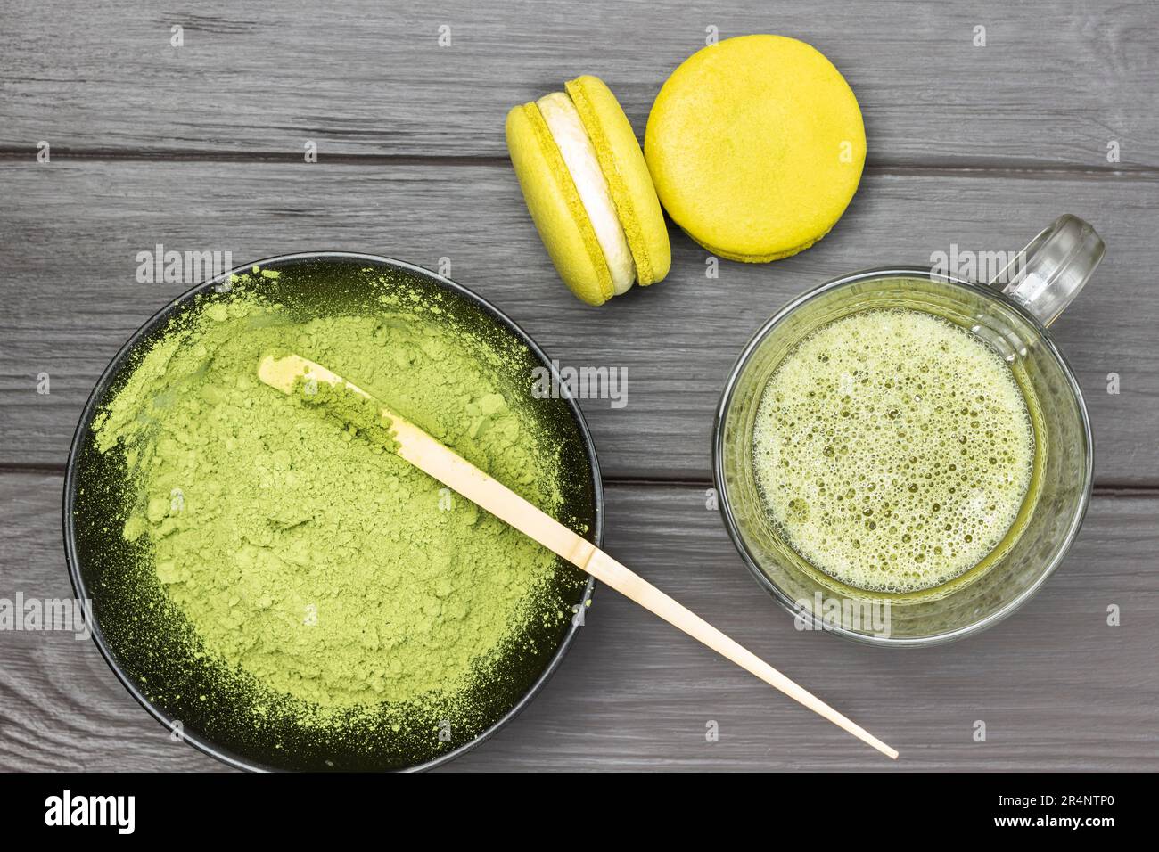 Two macaroni cakes and mug of matcha green tea. Measuring spoon in bowl with matcha powder. Dark wooden background. Stock Photo