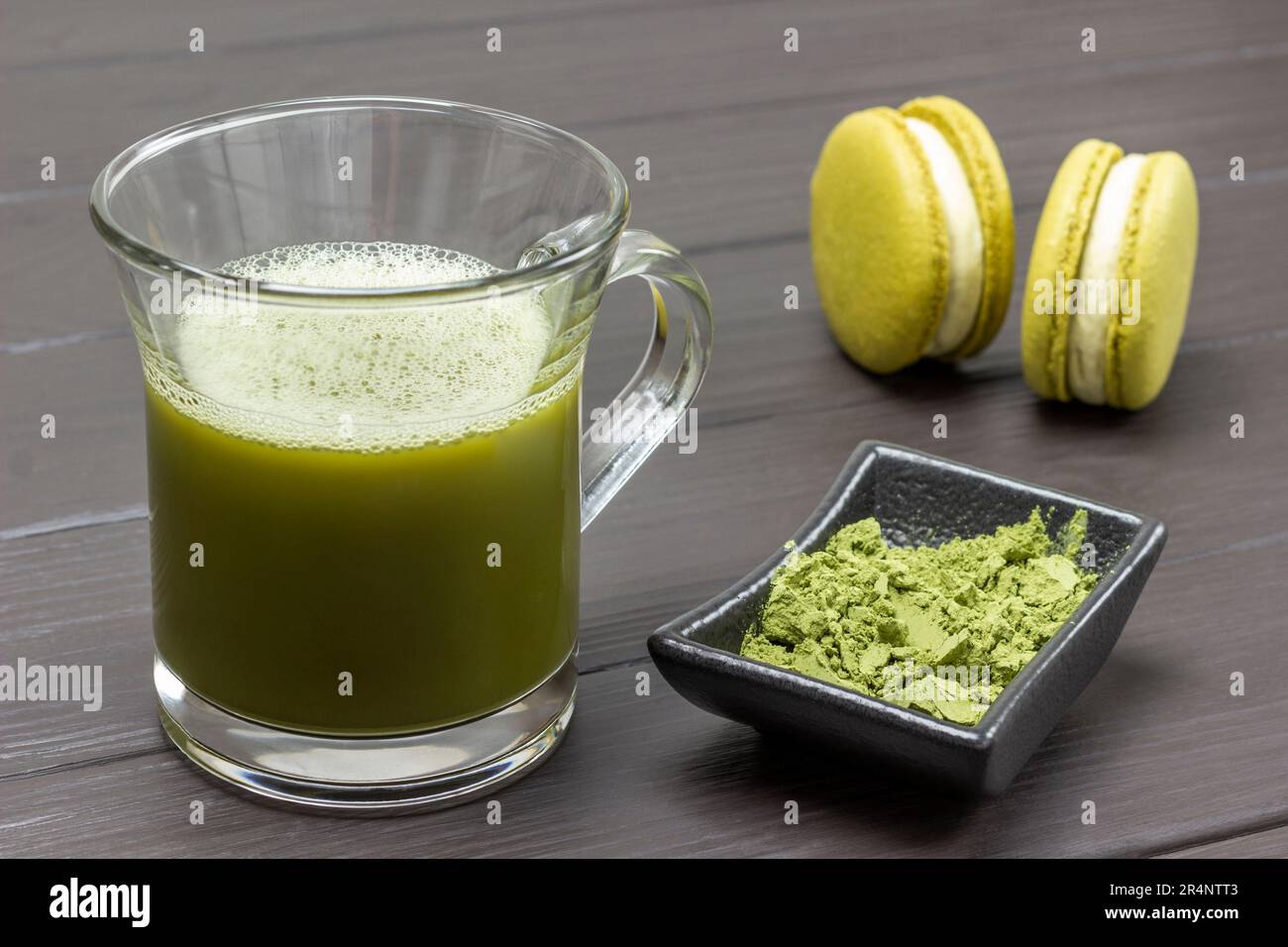 Mug of matcha green tea. Bowl with matcha powder and two macaroni cakes. Dark wooden background. Stock Photo