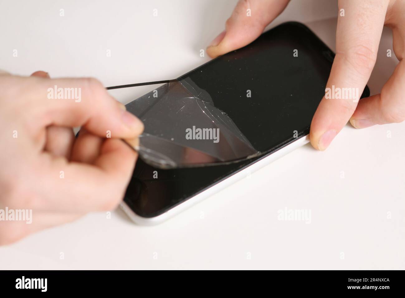 The man removes the old cracked protective glass from the phone. Broken protective glass Stock Photo