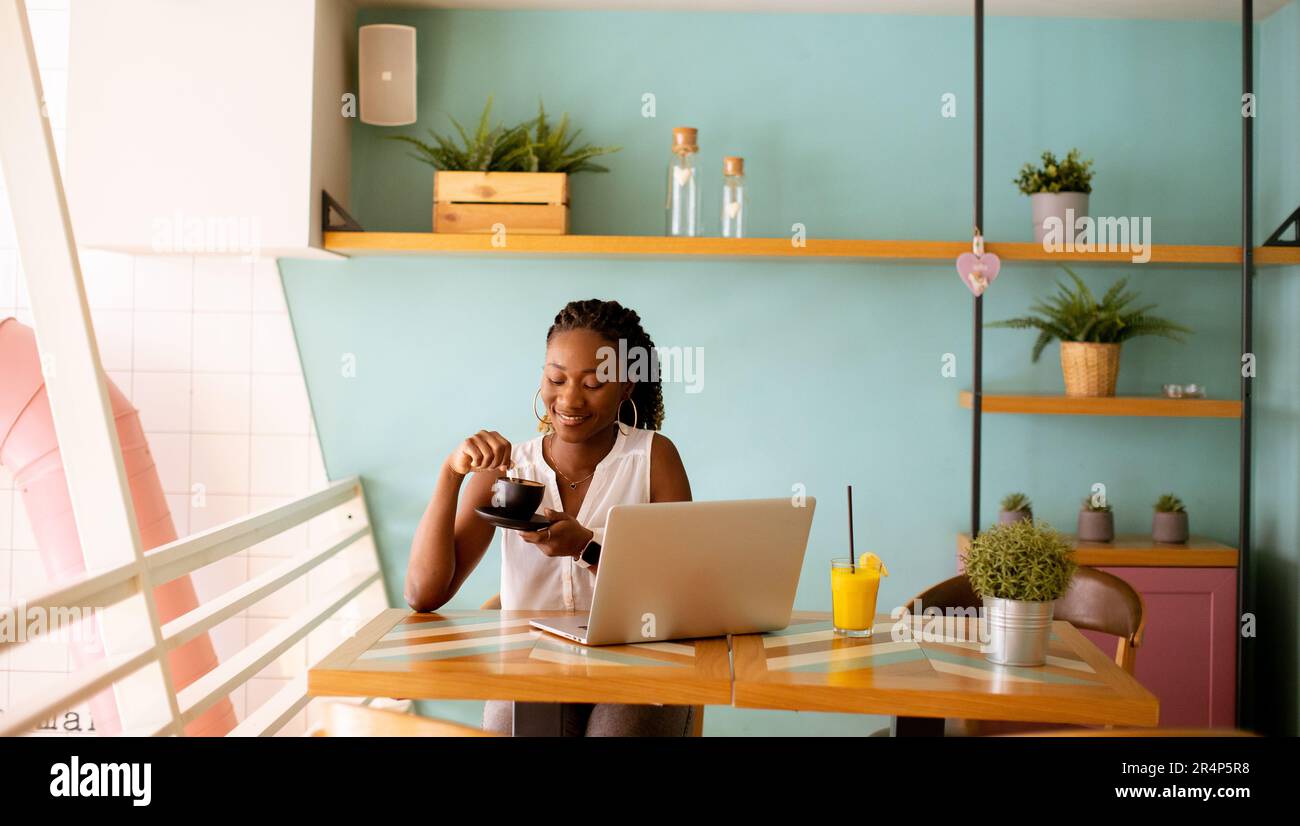 Pretty young black woman drinking coffee while working on laptop in the ...