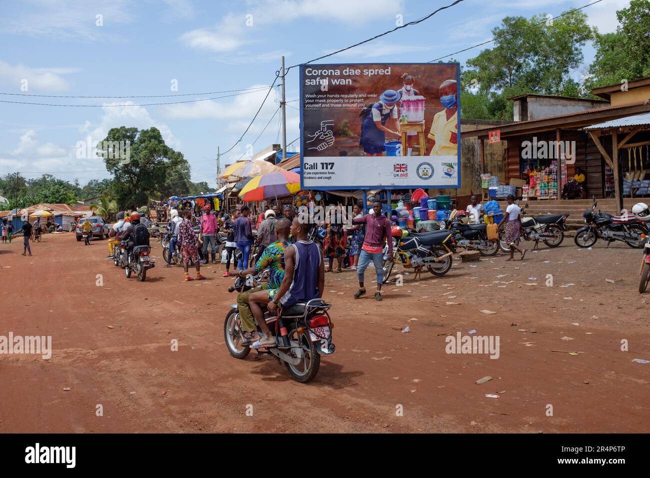 A billboard poster situated in a market in the town of Magburaka, Sierra Leone, promoting the control of Covid, and sponsored by UK Aid Stock Photo