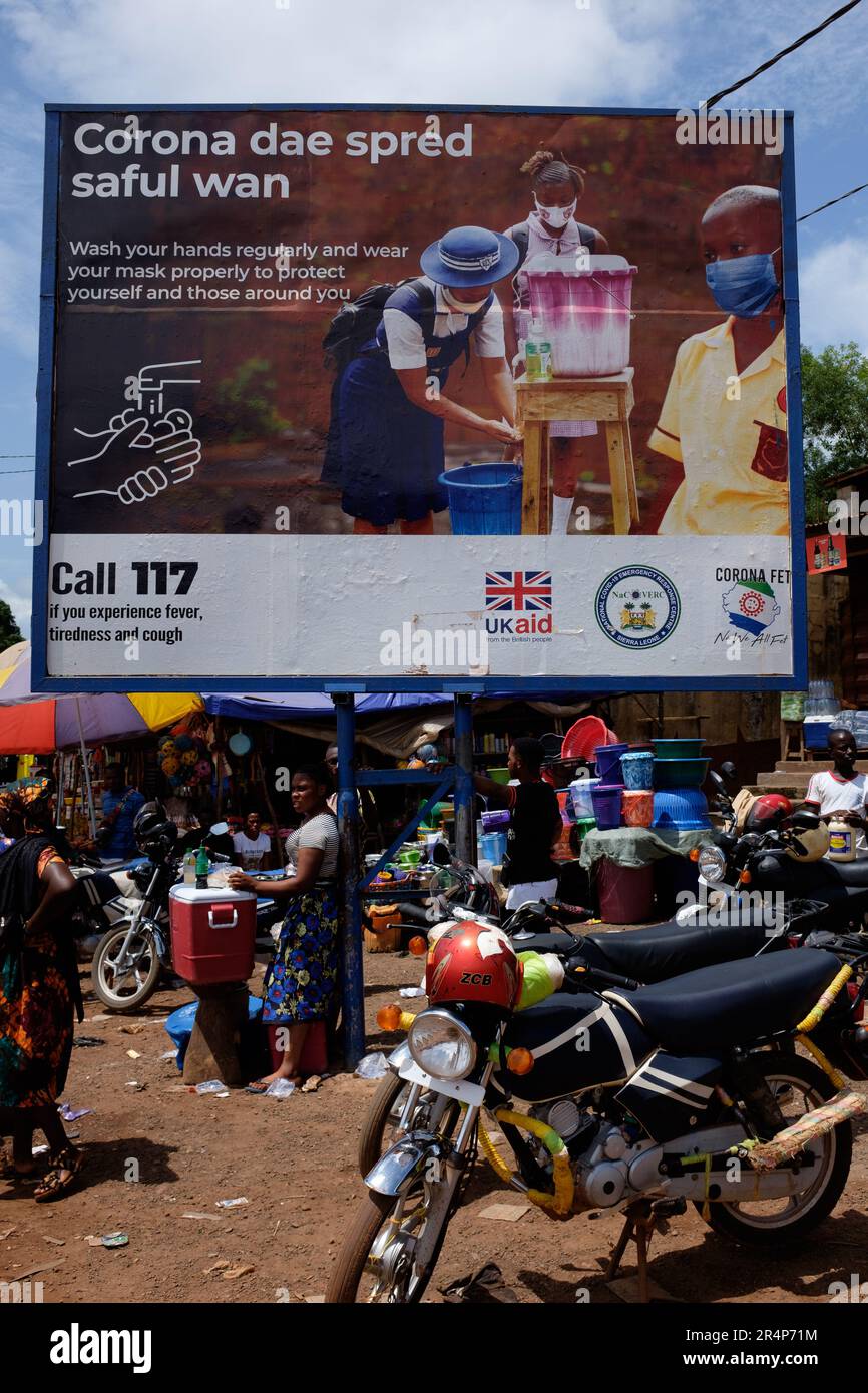 A billboard poster situated in a market in the town of Magburaka, Sierra Leone, promoting the control of Covid, and sponsored by UK Aid Stock Photo