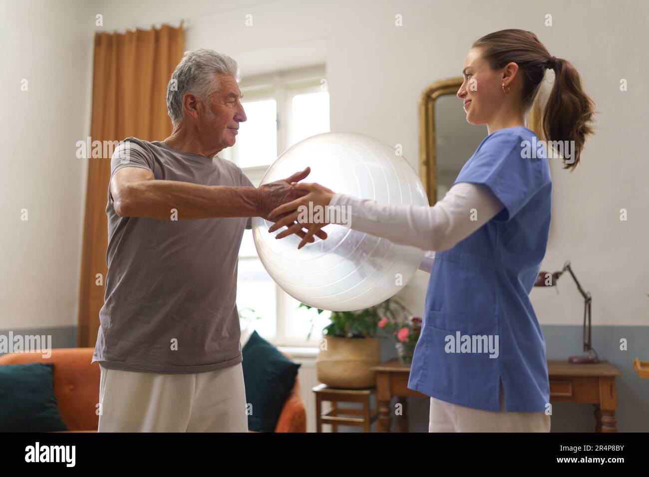 Young physiotherapist helping senior man to do exercise with fit ball ...