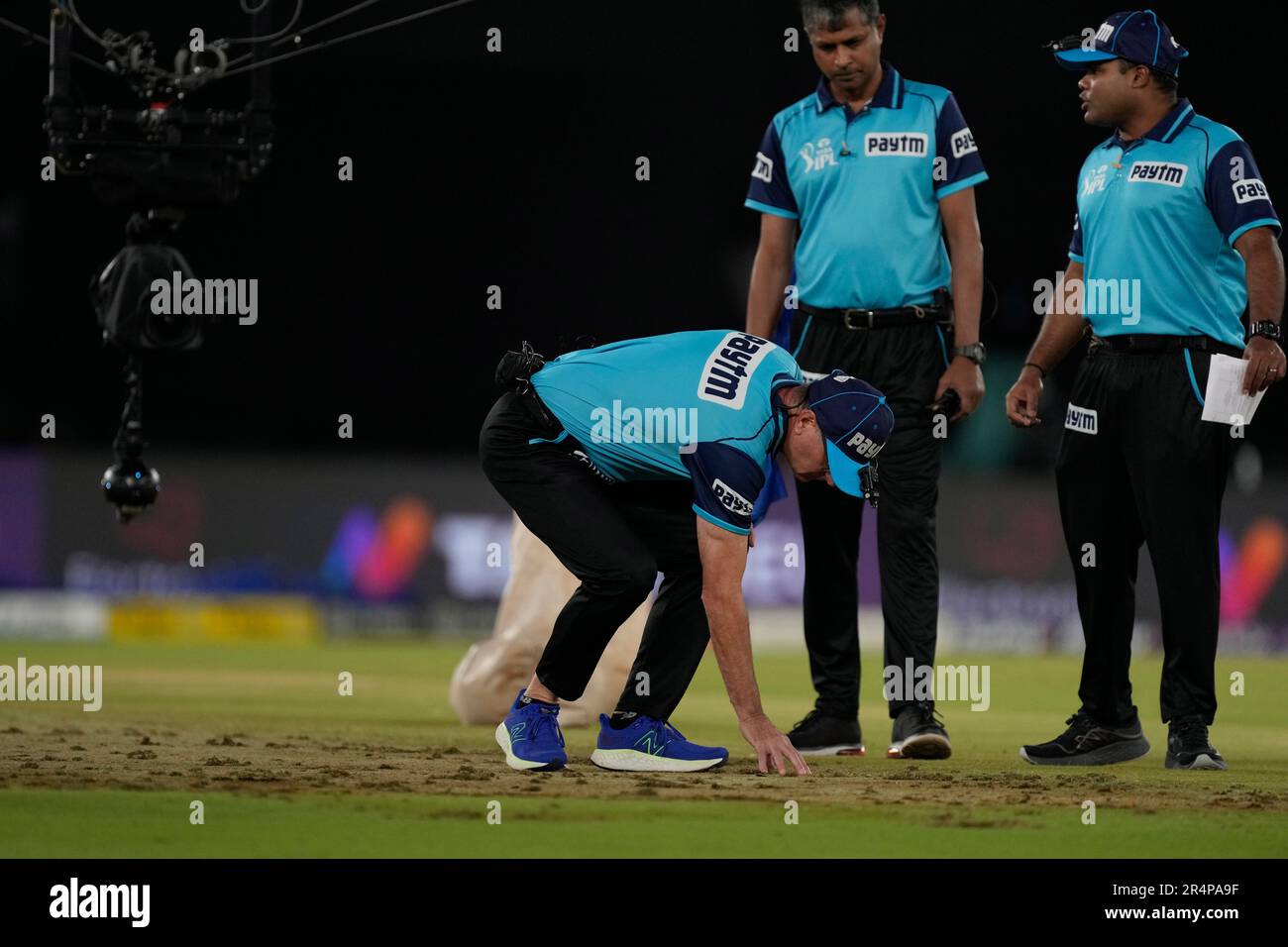 An umpire touches the ground to inspect the wet patches in the pitch