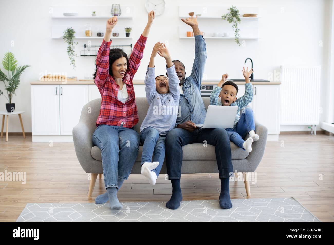 Emotional multiracial people raising arms high in air while watching online football match on laptop at home
