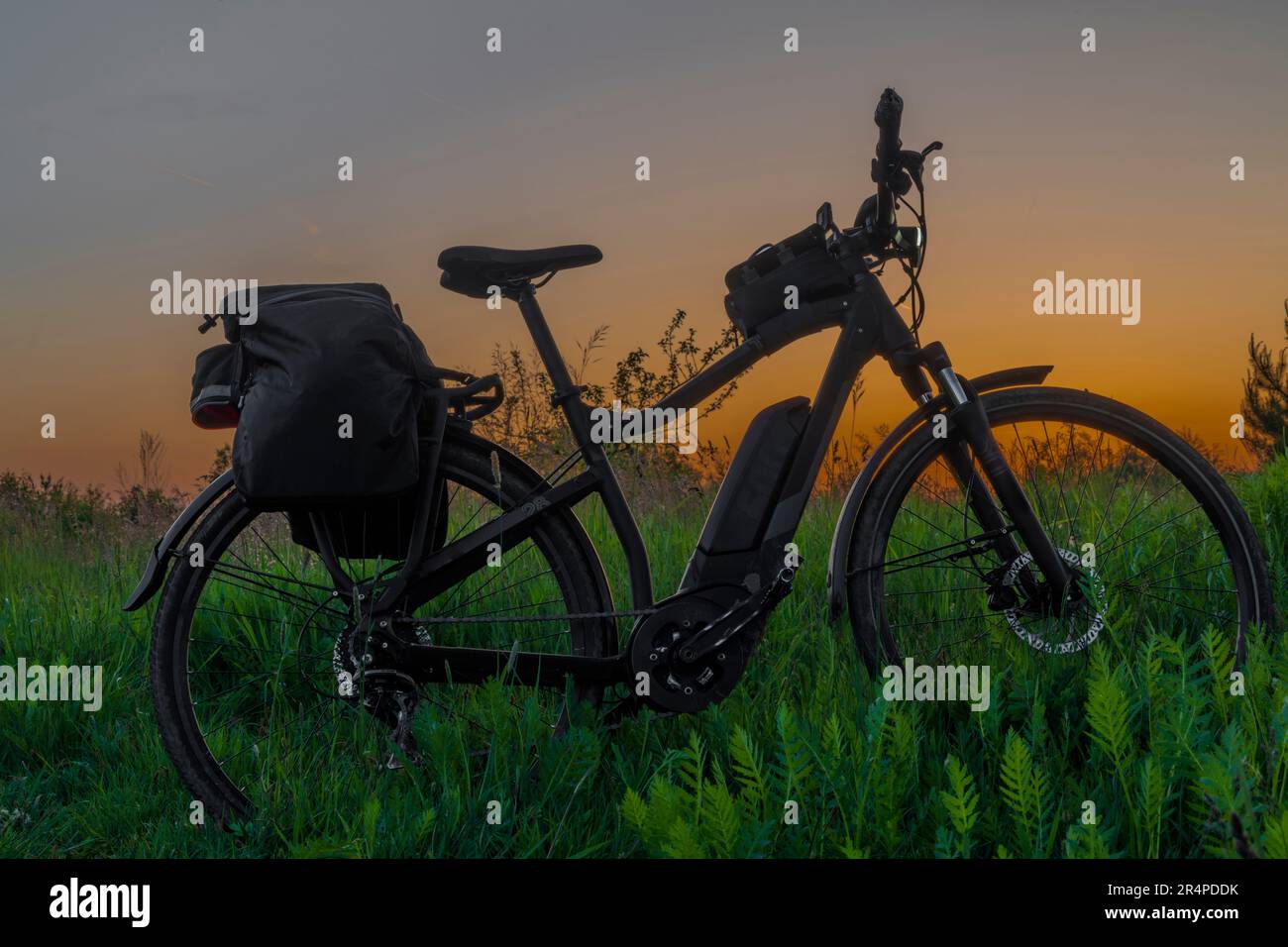 Electric bike with black bag on overgrown meadow with after sunset orange sky Stock Photo