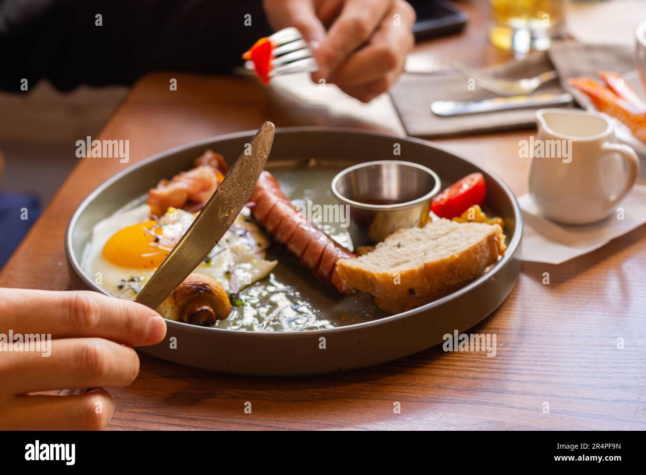 Hands with knife and fork and continental breakfast. Man eating fried