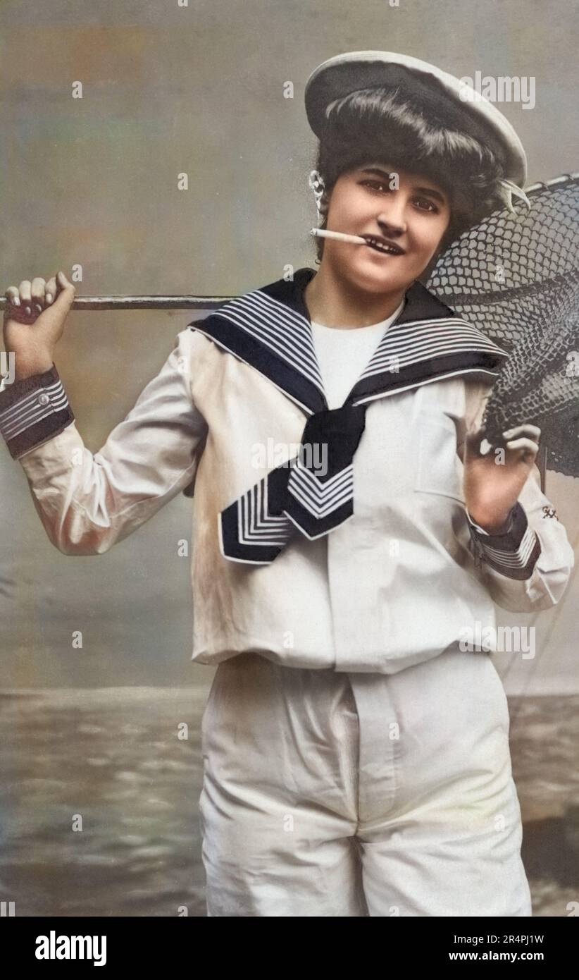 Vintage photographic postcard of a young girl wearing sailor type clothing and holding a fishing net while smoking a cigarette, circa 1910-1915, colorized. Stock Photo