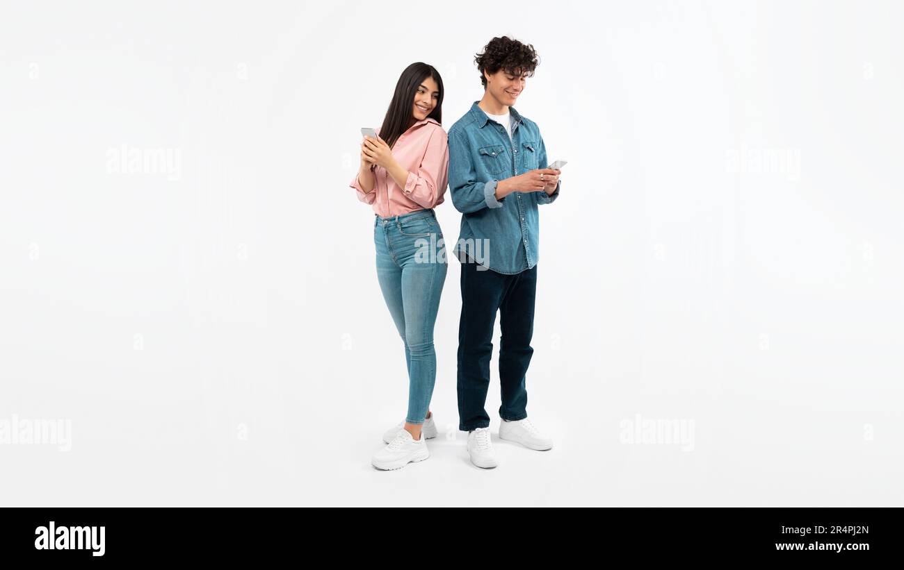 Young Couple Using Mobile Phones Texting Standing On White Background Stock Photo