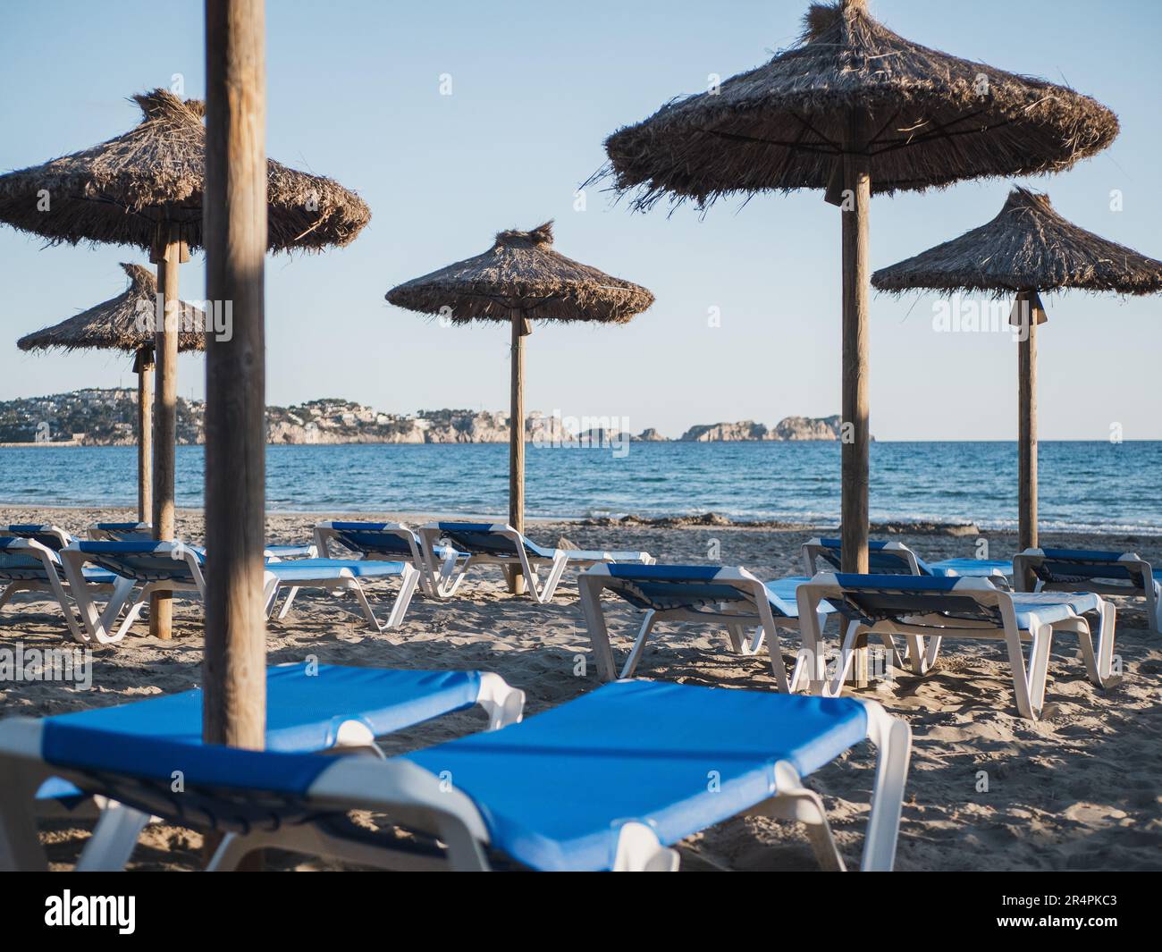 Sandy beach with blue sunbeds and straw umbrellas and the sea at the background. Mediterranean beach Gran Tora in Paguera, Calvia Stock Photo