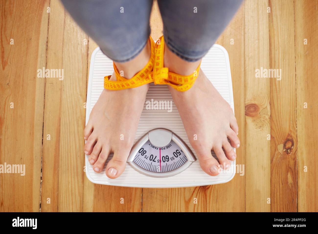 https://c8.alamy.com/comp/2R4PP2G/female-feet-on-white-scales-tied-up-with-measuring-tape-2R4PP2G.jpg