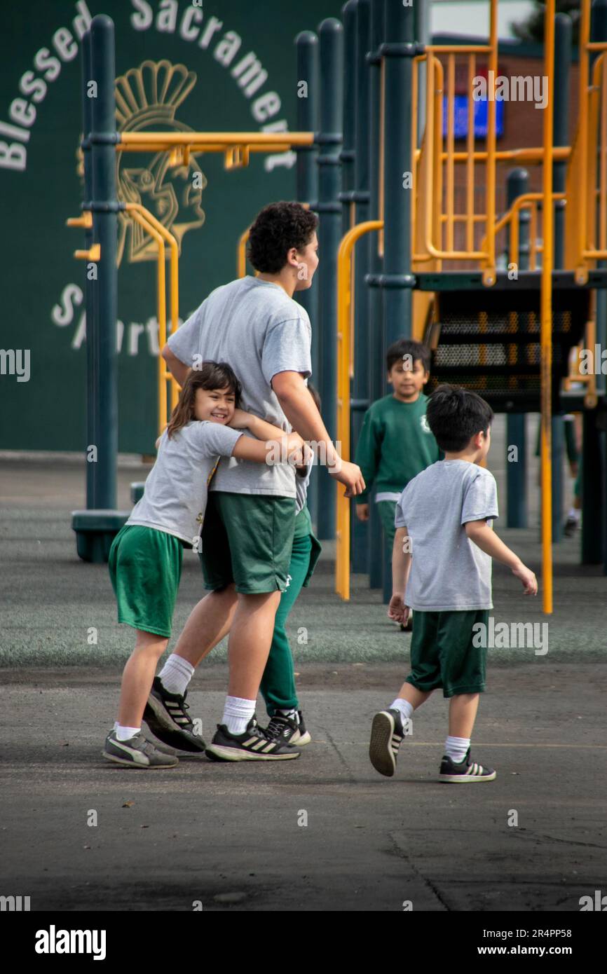 An elementary student at a Southern California Catholic school hugs her older brother during recess in the school yard playground. Stock Photo