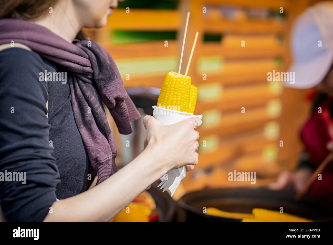 Cooked sweet corn on stick in hand of girl, selective focus. Summer vegan dinner or appetizer, grilling Stock Photo